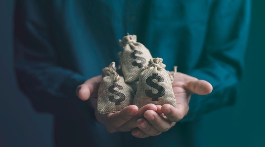 Businessman holding money bags_shutterstock_2380582577 900x500