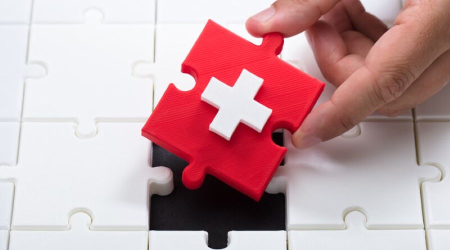 red cross puzzle piece amongst white puzzle pieces_canstockphoto59692997-2 900x500